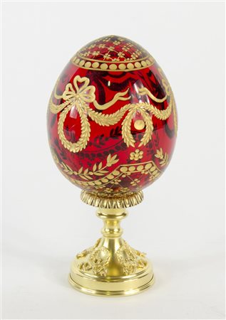 Modello di uovo in vetro rosso con decori incisi a dorature su base in bronzo...