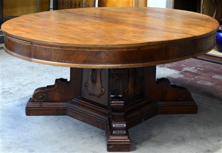 Grande tavolo allungabile di forma tonda con fascia lastronata in noce, gamba...