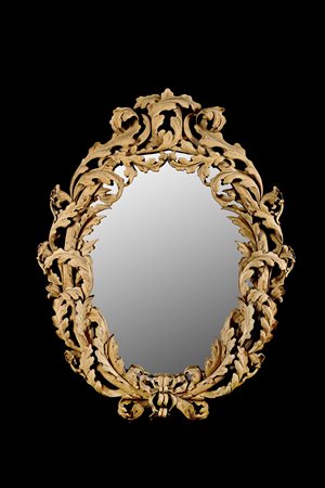 Specchiera di forma ovale con cornice in legno riccamente intagliata e...