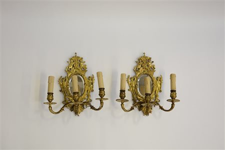 Coppia di appliques a tre fiamme in metallo dorato con fondo a specchio entro...