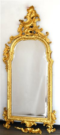 Specchiera di forma sagomata in legno intagliato e dorato a volute fogliate e...
