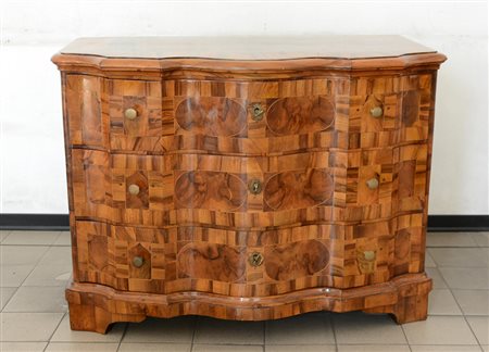 Antico cassettone di forma mossa a tre cassetti pannellati in radica, piedi a...