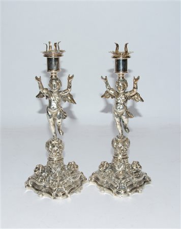 Coppia di candelieri in metallo argentato con fusto decorato a putti alati a...