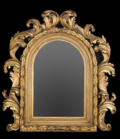 Specchiera in legno dorato, con cornice ad arco modanata, racchiusa da foglie...