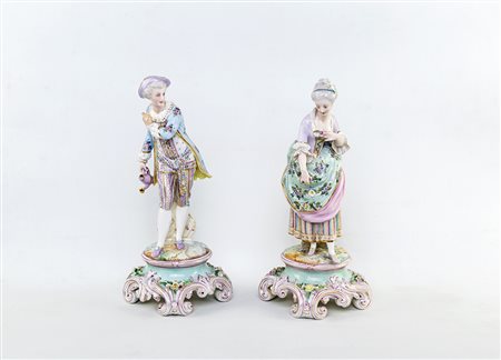 Coppia di figure in porcellana policroma raffiguranti due giovani in abiti...
