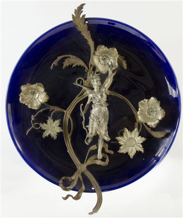 Grande piatto in porcellana con applicazione in metallo di donna alata. Diam....