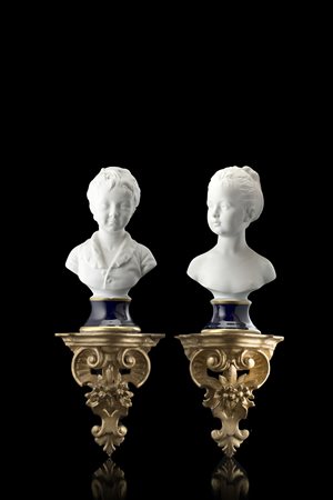 Due busti di fanciulli in biscuit su basi in porcellana blu poggianti su...