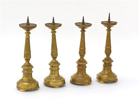 Gruppo di quattro candelieri ad una fiamma in ottone con base tornita. Fine...