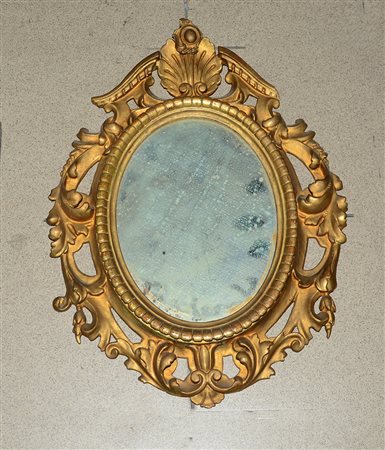Piccola specchiera di forma ovale in legno intagliato e dorato, decorata a...