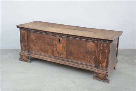 Cassapanca in noce con fronte intarsiato a stemma centrale, volute e figure...