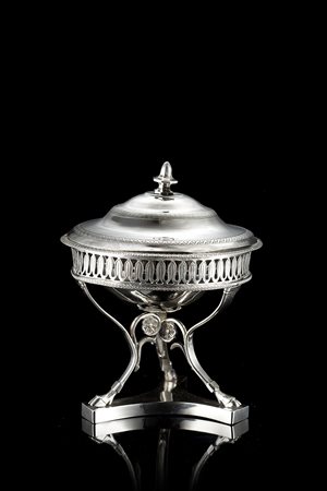 Zuccheriera in argento con corpo a bacile sorretto da tripode su plinto...