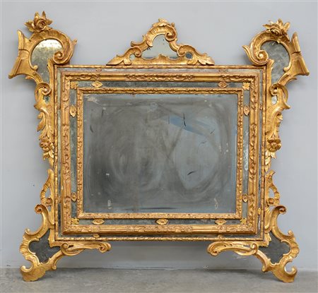 Antica specchiera di forma sagomata in legno intagliato e dorato decorata a...