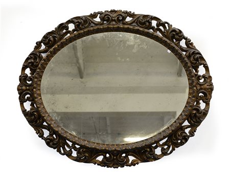 Specchiera ovale con cornice in legno intagliato e traforato a volute...