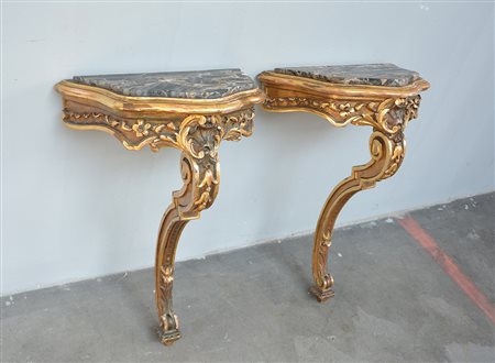 Coppia di consolles in legno intagliato e dorato a motivi vegetali. Piani in...
