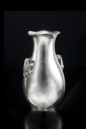 Vaso biansato in argento a corpo martellato. Anse in rilievo a volute....