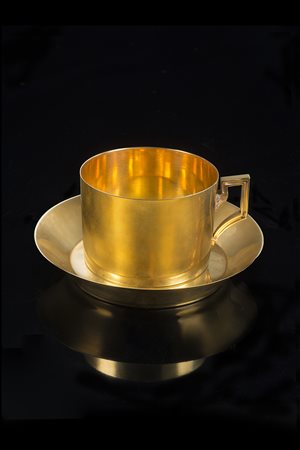 Tazza con piattino in oro ad un'ansa di forma squadrata, cesellata a motivi...
