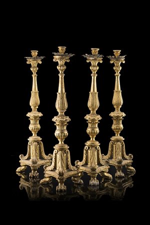 Gruppo di quattro torciere in legno intagliato e dorato, con fusto fogliato e...