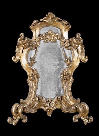 Specchiera in legno intagliato e dorato a volute fogliate e fiori. Cimasa con...