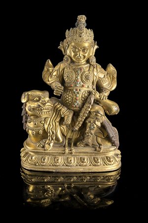 Divinità in bronzo dorato, raffigurata seduta su leone Buddhista su base a...