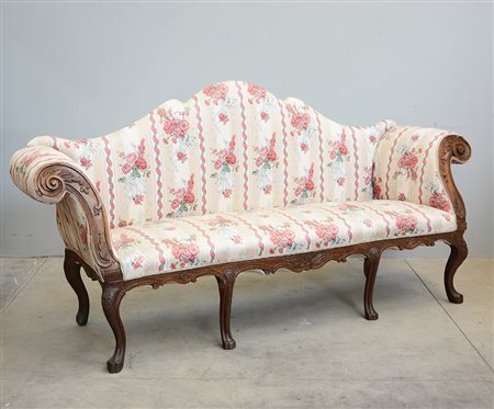 Divano a orecchioni in noce, intagliato a motivi vegetali, braccioli...