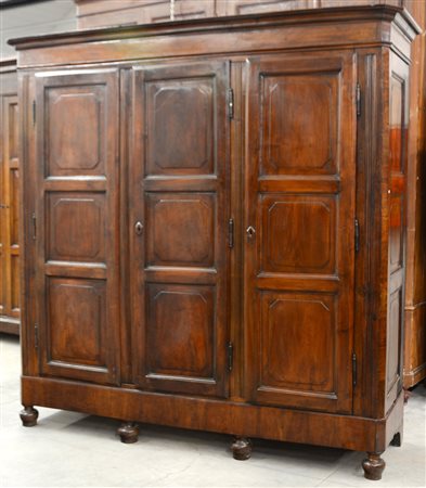 Armadio-guardaroba in noce a tre ante riquadrate con piedi torniti. Secolo...