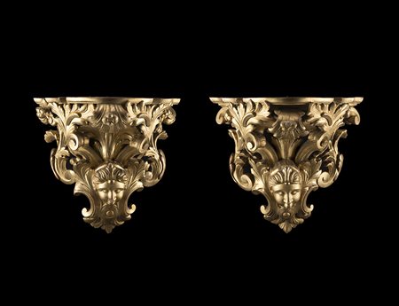 Coppia di mensole in legno intagliato e dorato a mascheroni, volute e fiori....