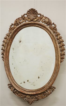 Specchiera di forma ovale intagliata e dorata a mecca, decorata con fregi a...