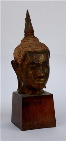 Testa di divinità buddista in bronzo dorato su base in legno (h cm 42)...