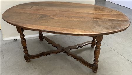 Tavolo da pranzo in noce con piano di forma ovale, gambe a rocchetto riunite...