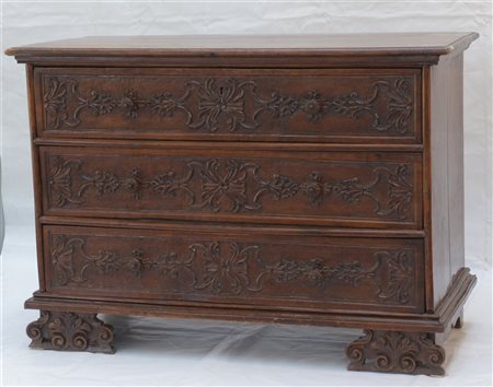 Comò in noce a tre cassetti intagliati a motivi vegetali, piedi a mensola....