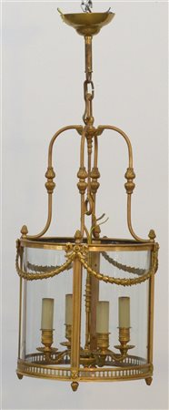 Lanterna a quattro luci in bronzo dorato e decorato a volute fogliate e nastri.