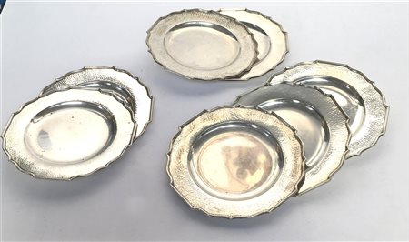 Gruppo di sette sottopiatti in argento con bordi sagomati e martellati. Titolo