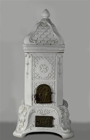 Stufa in maiolica parete color avorio con cimase, coronata da elemento a...