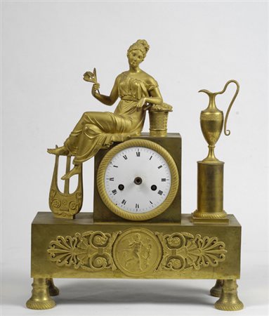 Orologio da tavolo in bronzo dorato, cassa a plinto sormontata da figura di...