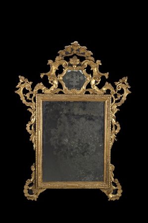 Specchiera in legno intagliato e dorato a volute e fiori, cimasa centrata da ca