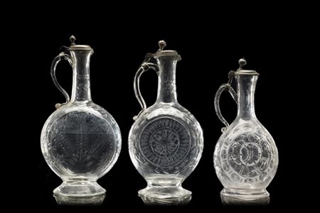 Tre caraffe in vetro con corpi incisi a motivi stilizzati, anse mosse, tappi in