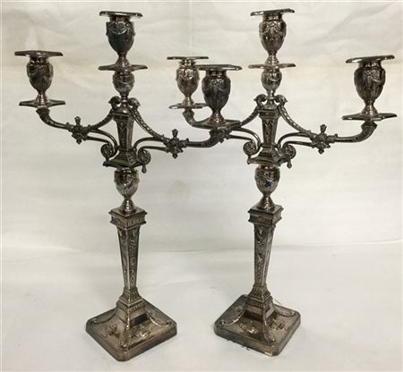 Coppia di candelieri a tre fiamme in metallo argentato decorato a volute, fogli