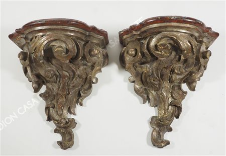 Coppia di mensole in legno argentato intagliate a volute. H. cm. 42.