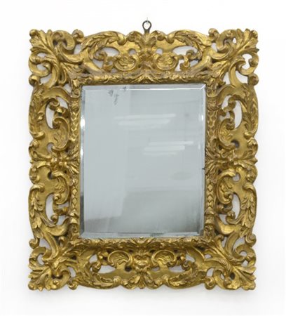 Specchiera in legno intagliato e dorato a volute fogliate sorrette da mascheron