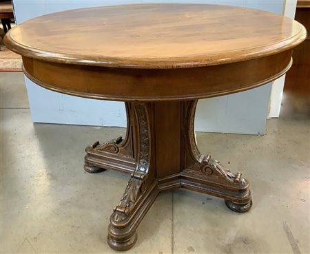 Tavolo tondo in noce con base a plinto e montanti intagliati, con piano in vetr