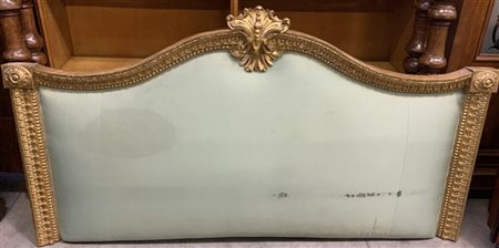 Testata da letto in legno dorato e intagliato a palmette, sormontata da rosoni.