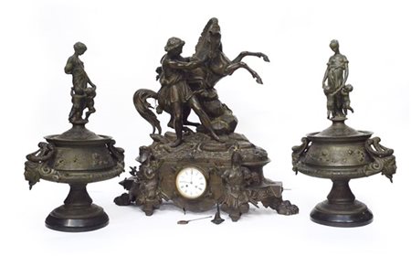 Trittico in metallo composto da orologio sormontato da figura con cavallo e due