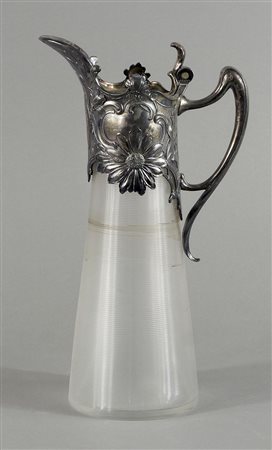 Brocca in vetro con collo e manico in metallo sbalzato a fiori. H. cm. 33.