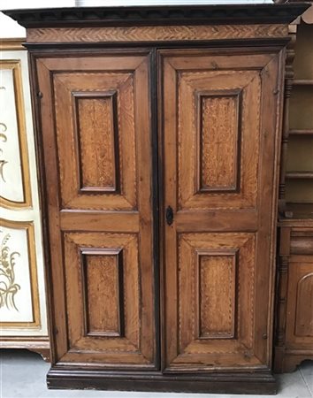 Antico armadio a due battenti con specchiature intarsiate a volute e motivi geo