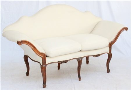 Divano a orecchioni in noce, fascia, montanti e gambe intagliate. Piedini a ric