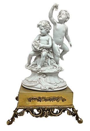 Porcellana in bisquit bianco raffigurante coppia di puttini e base in ottone dorato, XX secolo, firmato Benacchio. H cm 