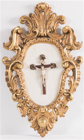 Crocifisso in materiale prezioso intagliato entro cornice lignea intagliata e...