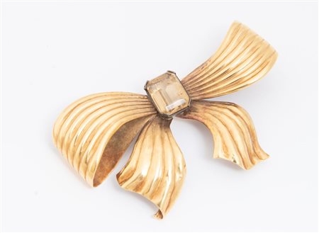 SPILLA IN ORO GIALLO modellata come un fiocco rigido in oro 18K, centrata da...