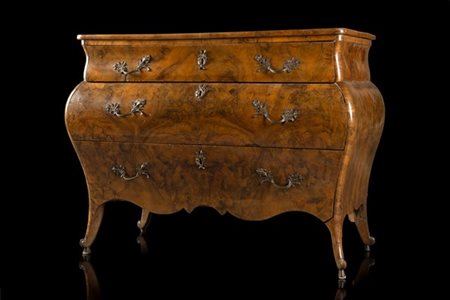 Comò di forma mossa e bombata lastronato in radica di noce. Fronte a due casset