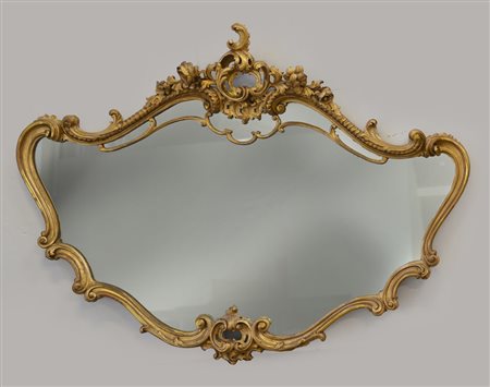 Specchiera di forma mossa in legno intagliato e dorato, cimasa a volute e fiori